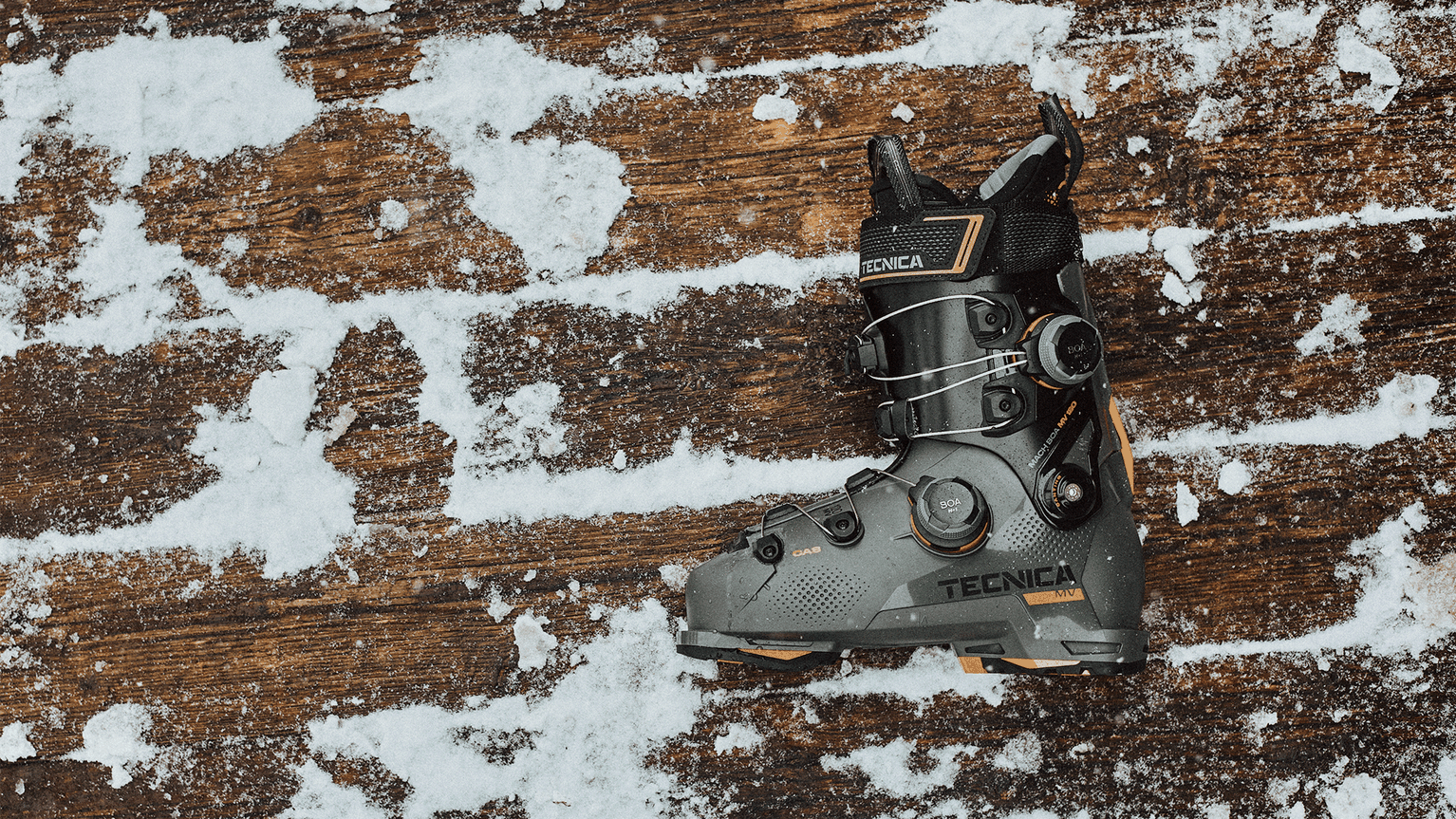 A single Tecnica ski boot on a snowy wooden surface, showcasing its design and details.