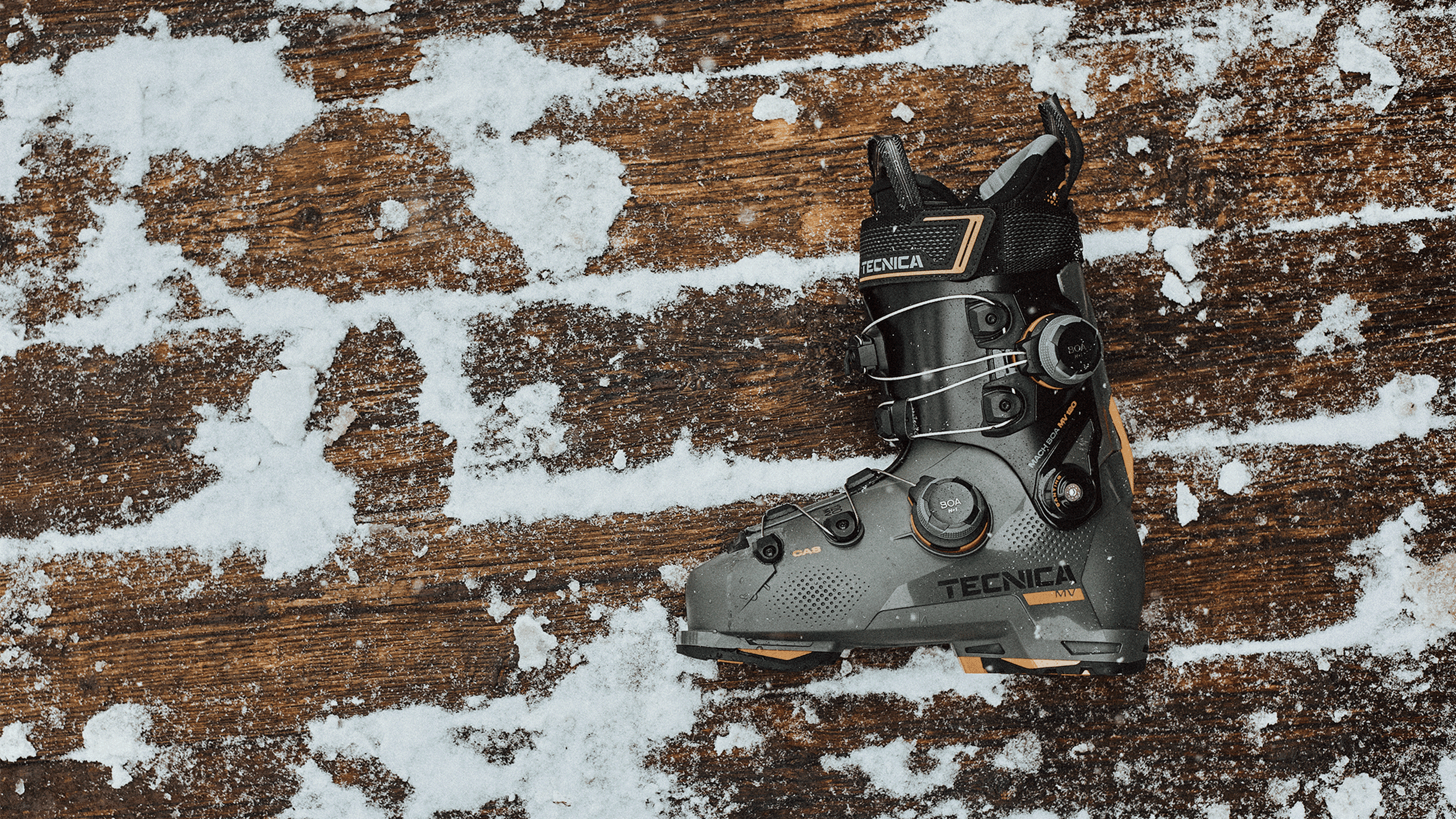 A single Tecnica ski boot on a snowy wooden surface, showcasing its design and details.