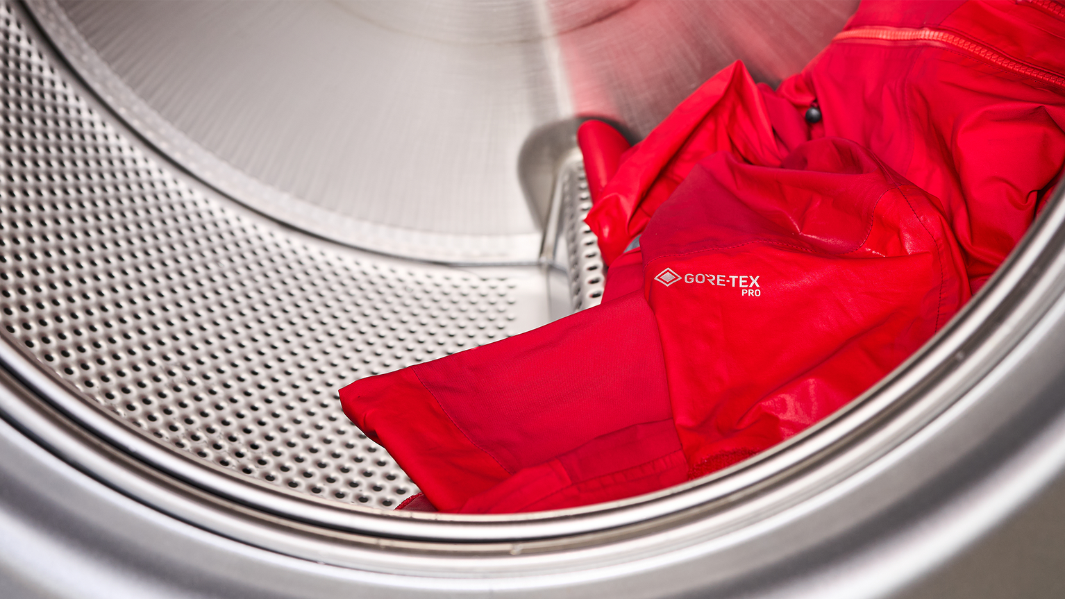 Red GORE-TEX Pro jacket inside a washing machine drum, partially visible in a stainless steel interior.