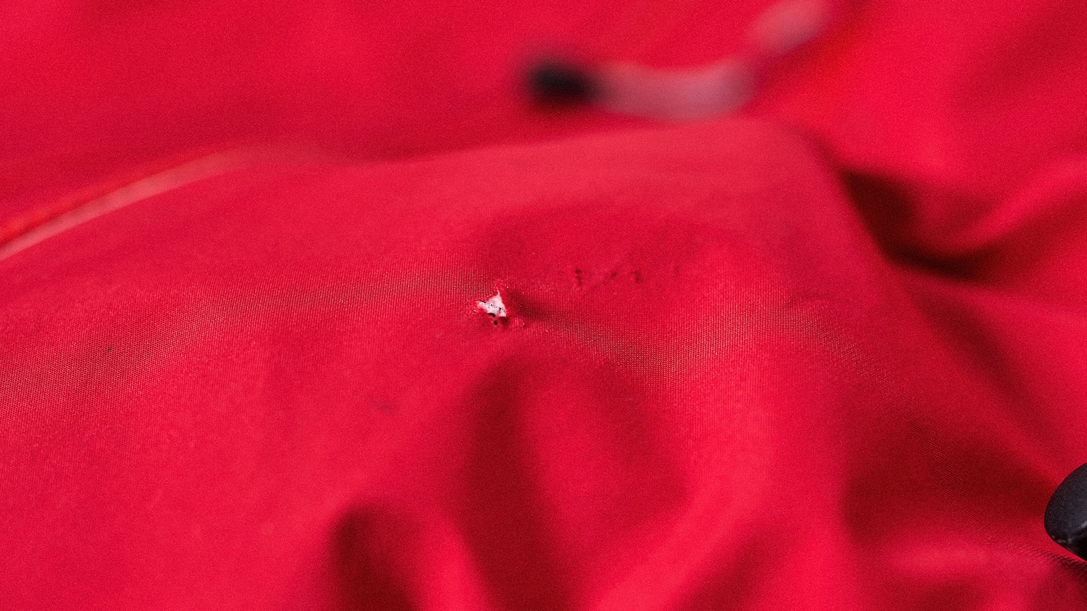 Close-up of a red waterproof jacket with a small hole and slight fraying, showing texture and wear.