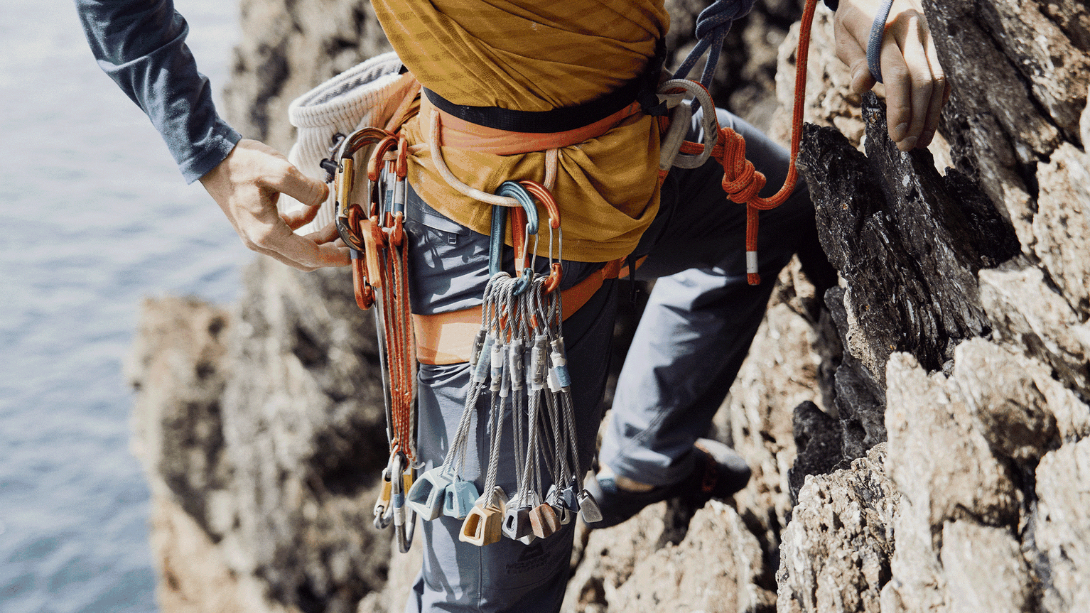Rock climber scaling a cliff, wearing a harness with carabiners and ropes attached.