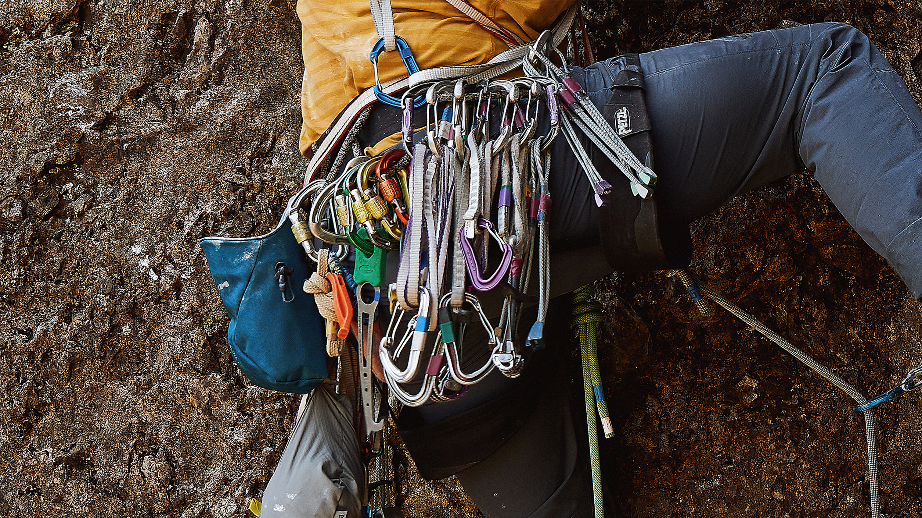 Climber scales a rock face, equipped with an array of carabiners, ropes, and climbing gear attached to their harness for a challenging ascent.