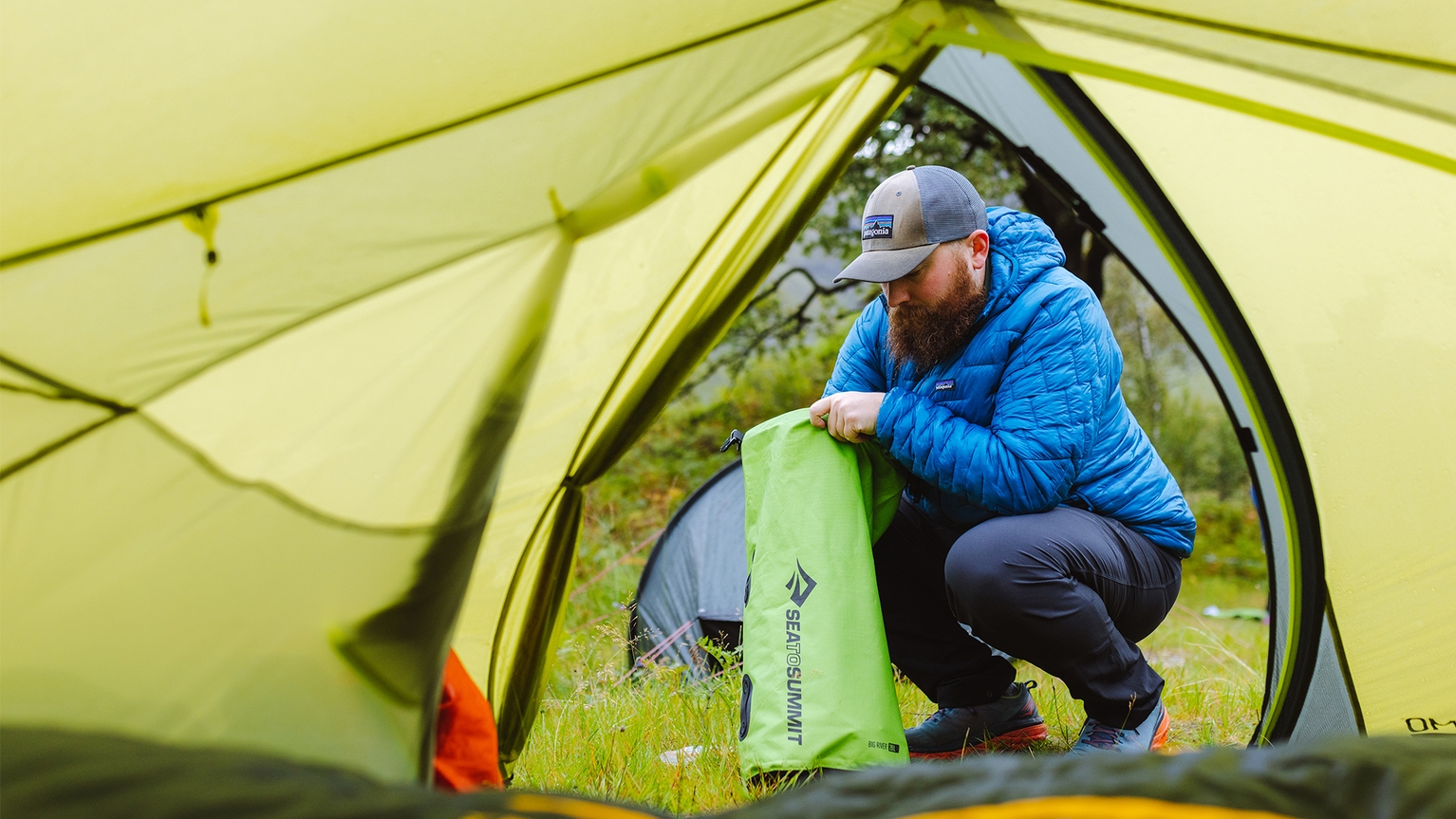man crouched outside tent packing a dry bag