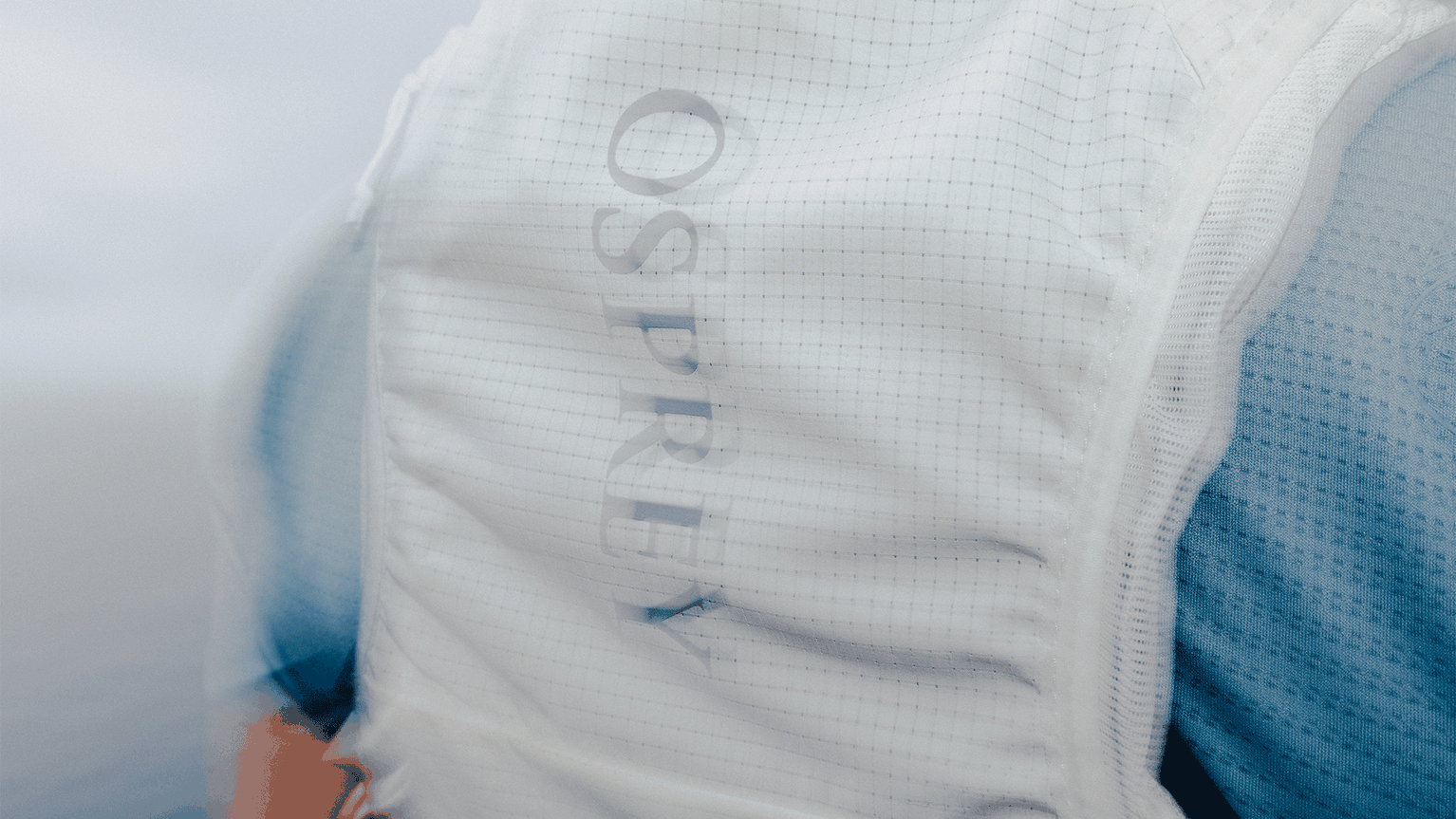 Close-up of a white Osprey branded padded vest with a grid pattern, on a person wearing a blue garment.