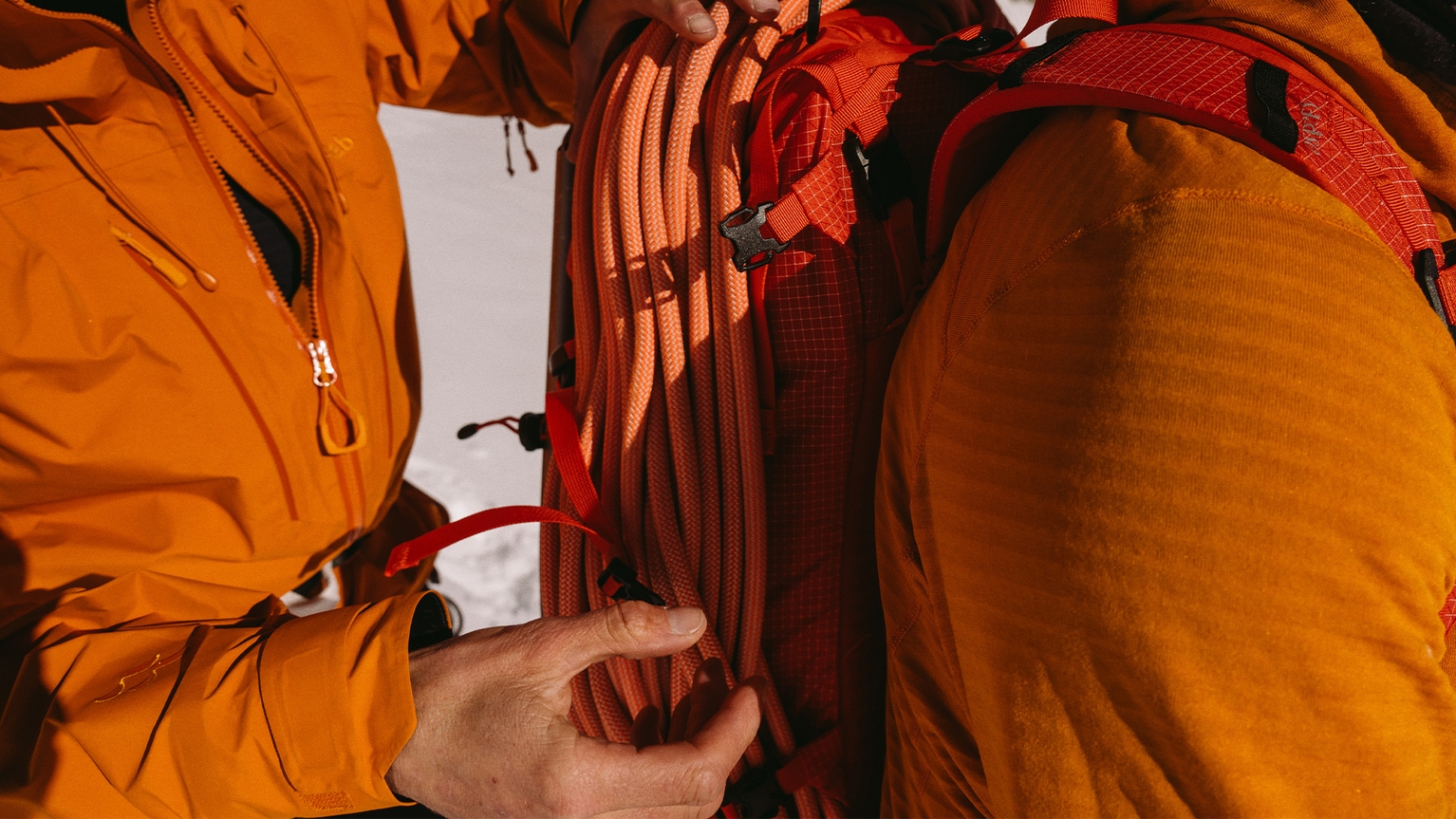 two climbers dressed in orange climbing gear. One helping the other with ropes.