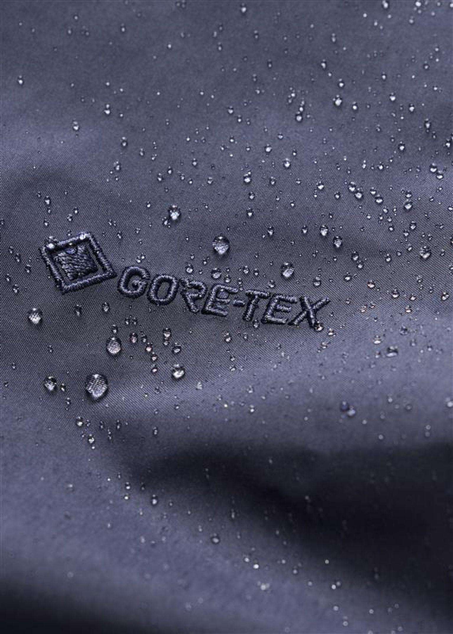 Close-up of water droplets on a dark Gore-Tex fabric surface, showcasing its water-resistant properties.
