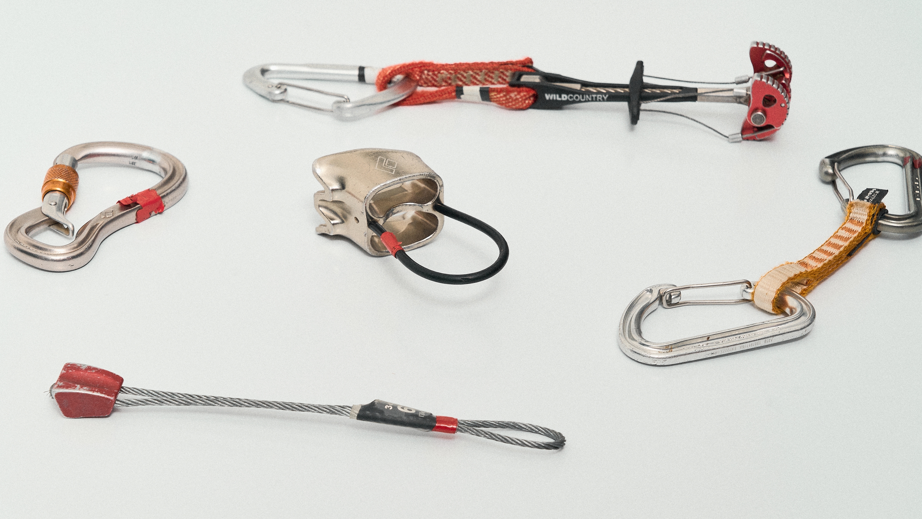Various climbing gear, including carabiners and a cam, arranged on a white surface.