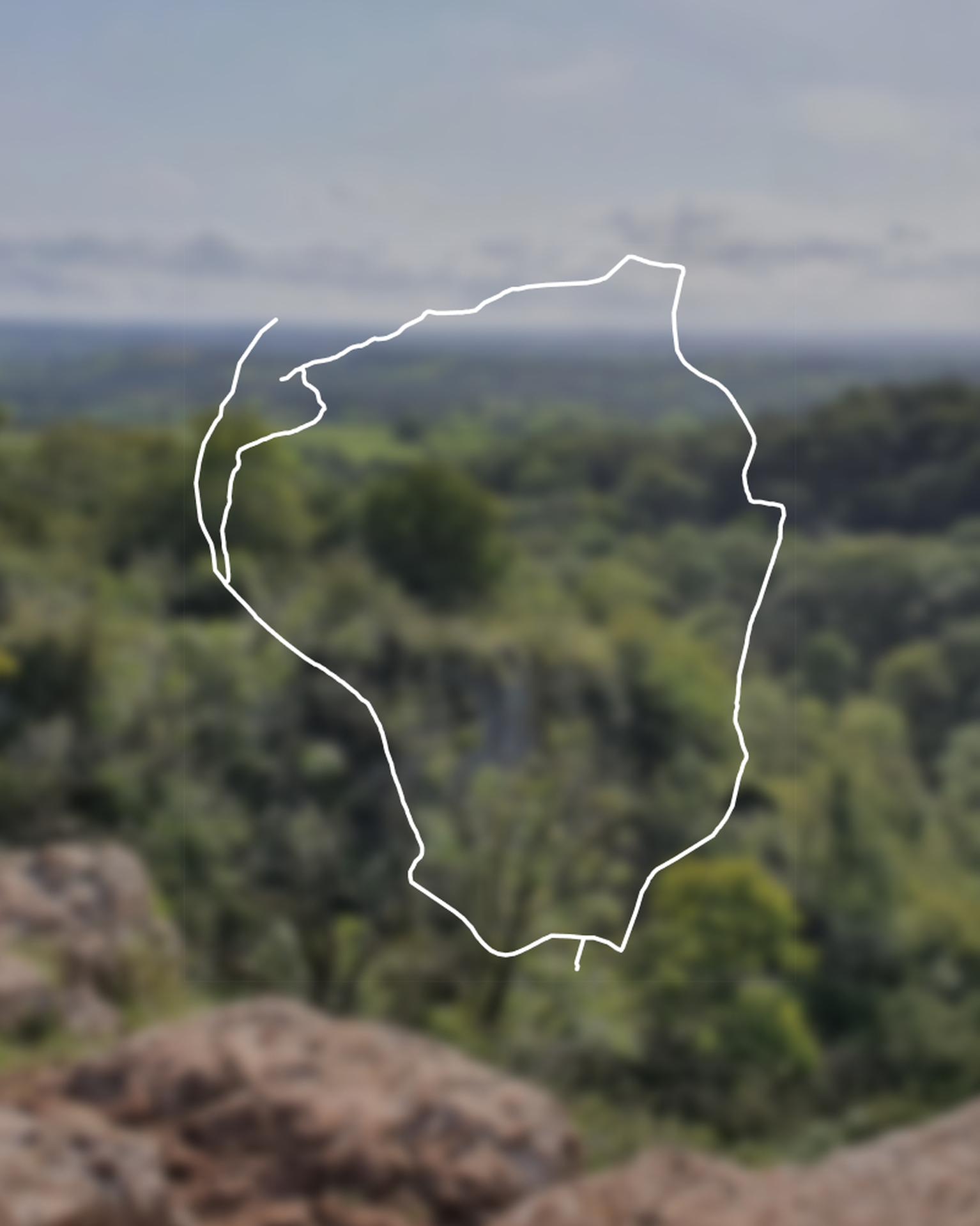 Outline of a hiking route over a blurred forested landscape with a cloudy sky in the background.