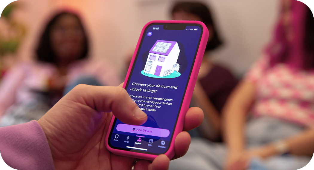 A person holds a smartphone with an app interface, while two people sit blurred in the background.