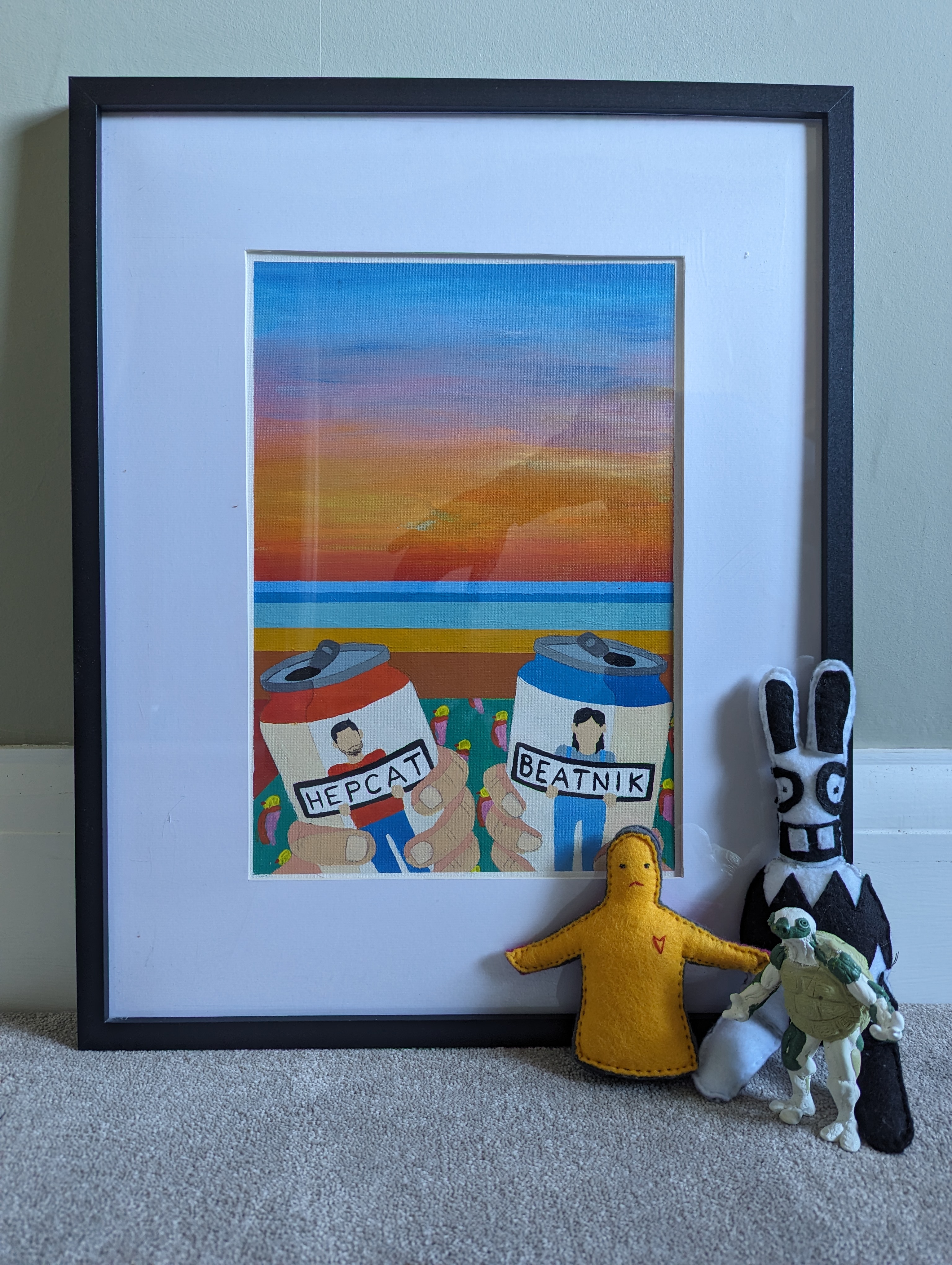 Photograph of various toys leaning up against a framed painting of beer with a sunset in the background
