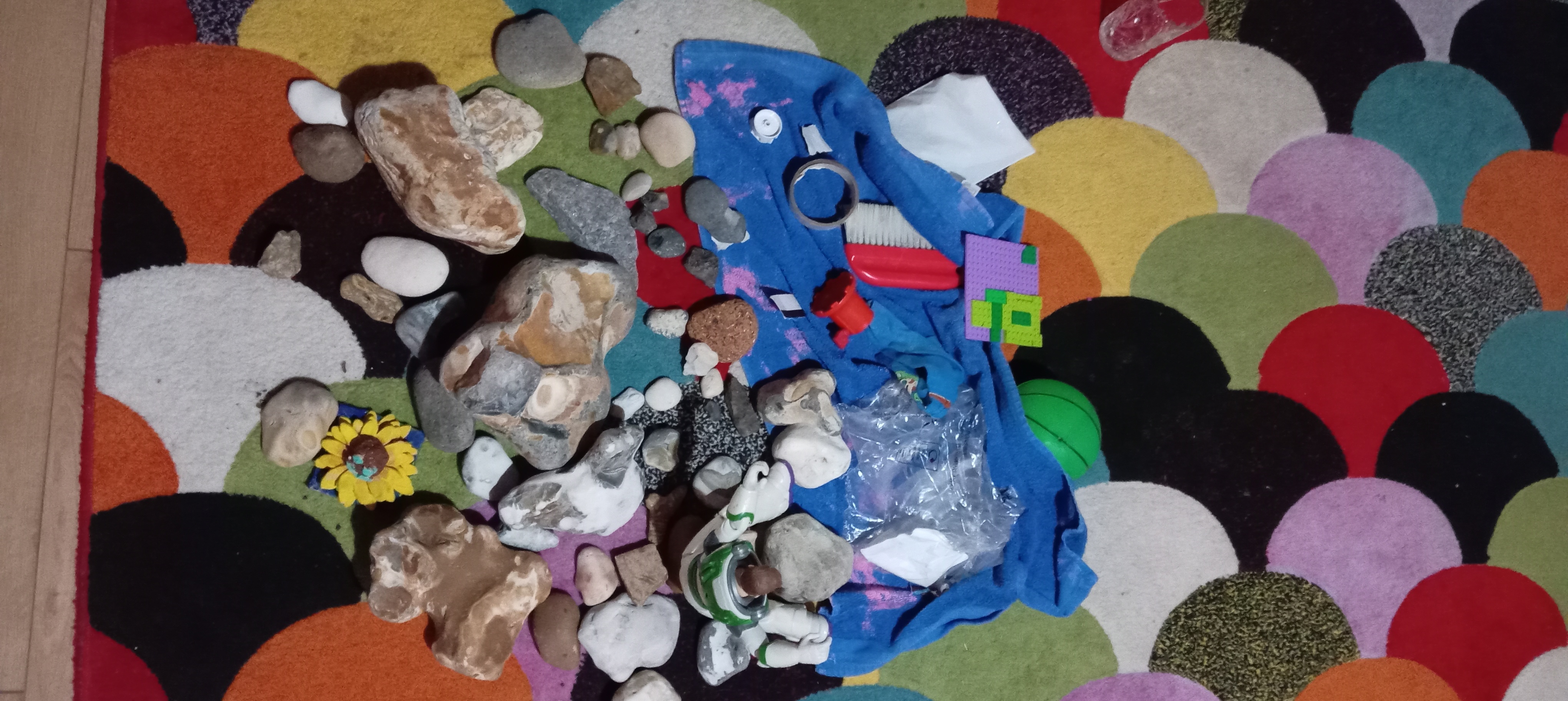A colorful carpet with various rocks, small toys, a sunflower ornament, and scattered items on a blue cloth.