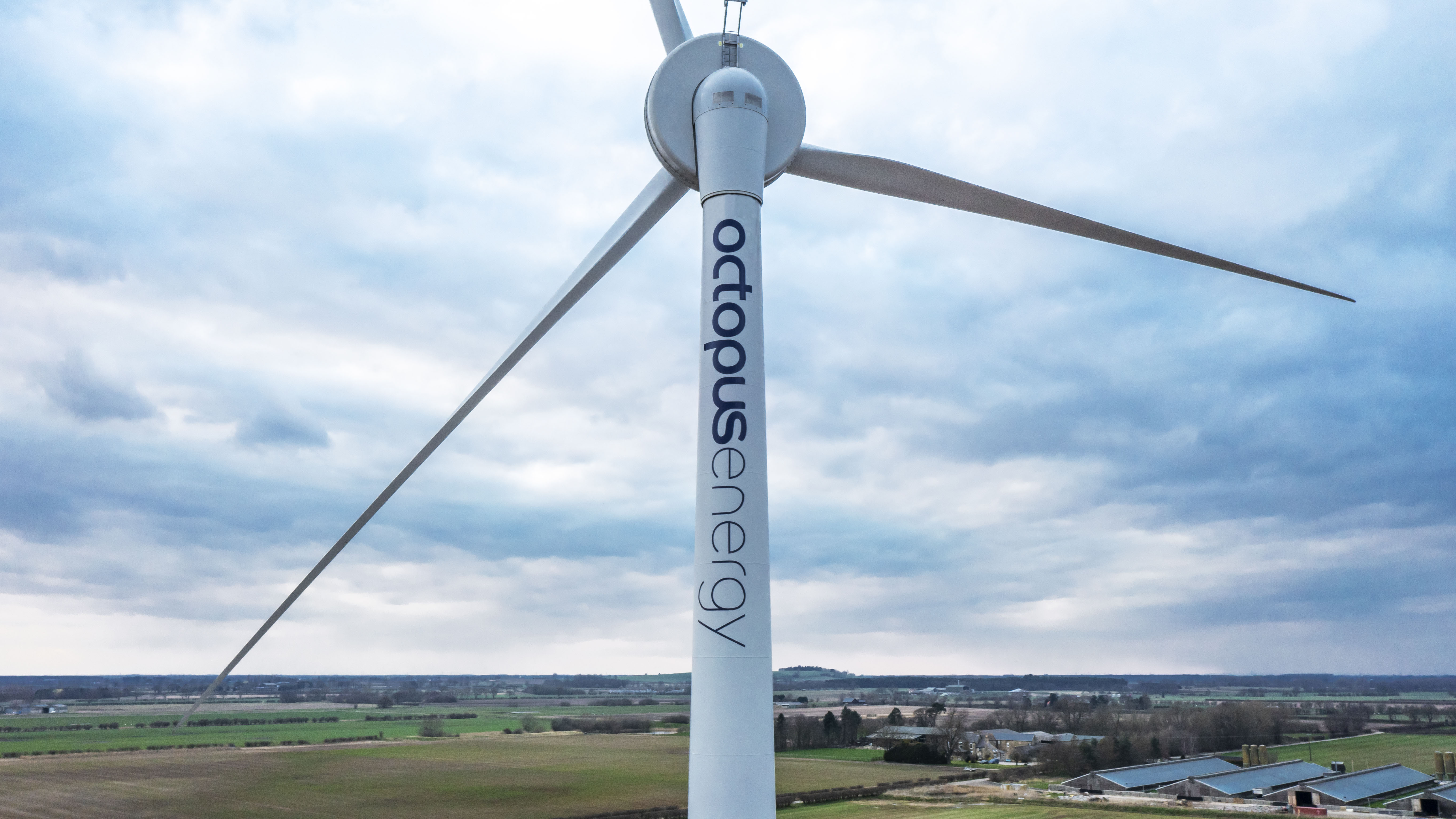 A large wind turbine with "Octopus Energy" written on the tower, set against a cloudy sky and a rural landscape.