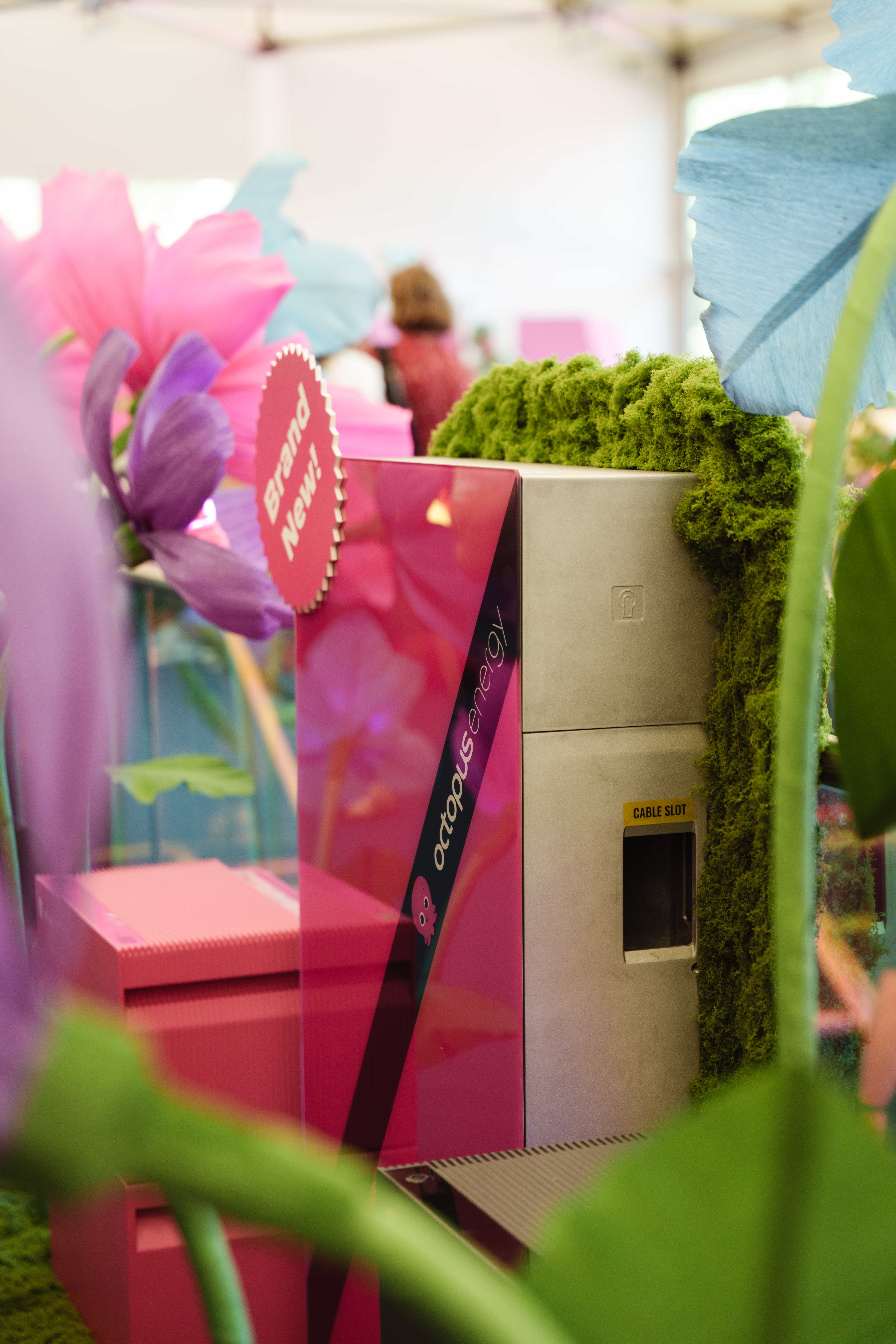 Pink and green energy booth with "octopus energy" branding, surrounded by oversized artificial flowers and greenery.
