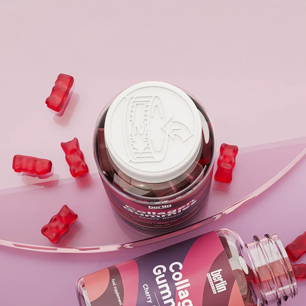 A close-up of two transparent plastic bottles of collagen gummies on a pink surface. One bottle is upright with a white child-resistant cap featuring embossed instructions and an arrow. The other bottle lies on its side, partially open, showing the label that reads “Collagen Gummies” and “Cherry.” Several red gummy bears are scattered around the bottles.