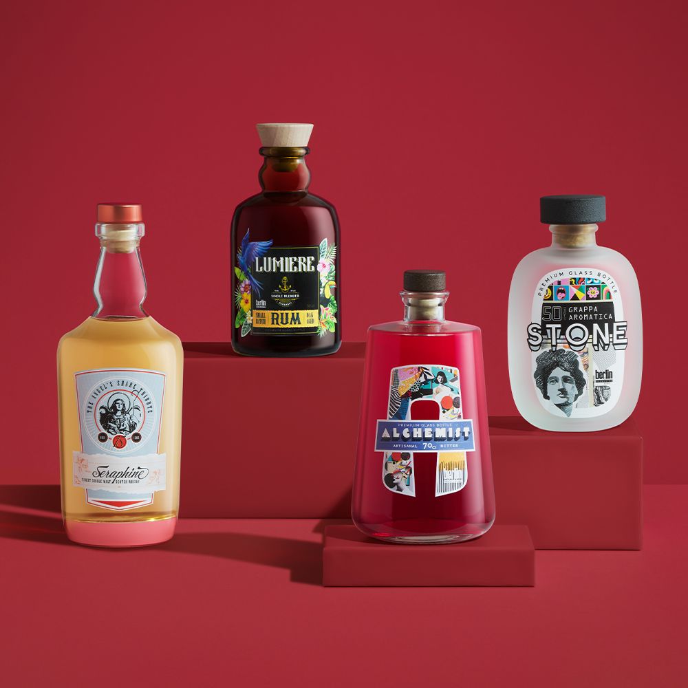 Modern Classics collection by Berlin Packaging featuring Seraphine, Lumière, Alchemist and Stone glass bottles for distilled spirits, showcasing distinctive silhouettes, premium closures and creative label designs on a red display setting.