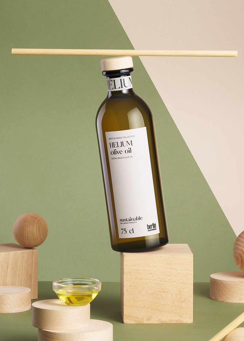 Labelled Helium olive oil bottle on geometric wooden shapes with green and beige background. A small dish with oil is nearby.