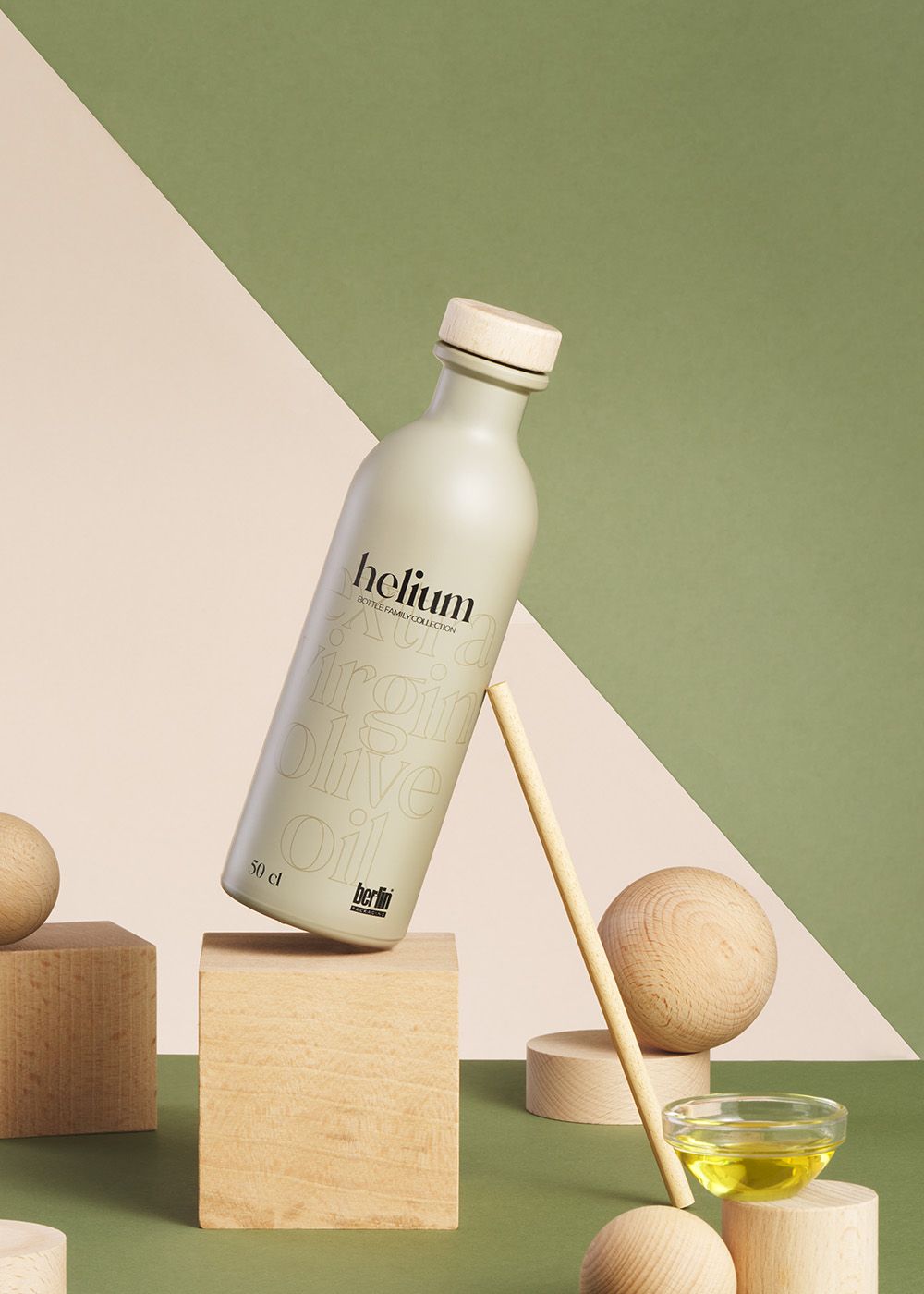 decorated Helium olive oil bottle on geometric wooden shapes with green and beige background. A small dish with oil is nearby.
