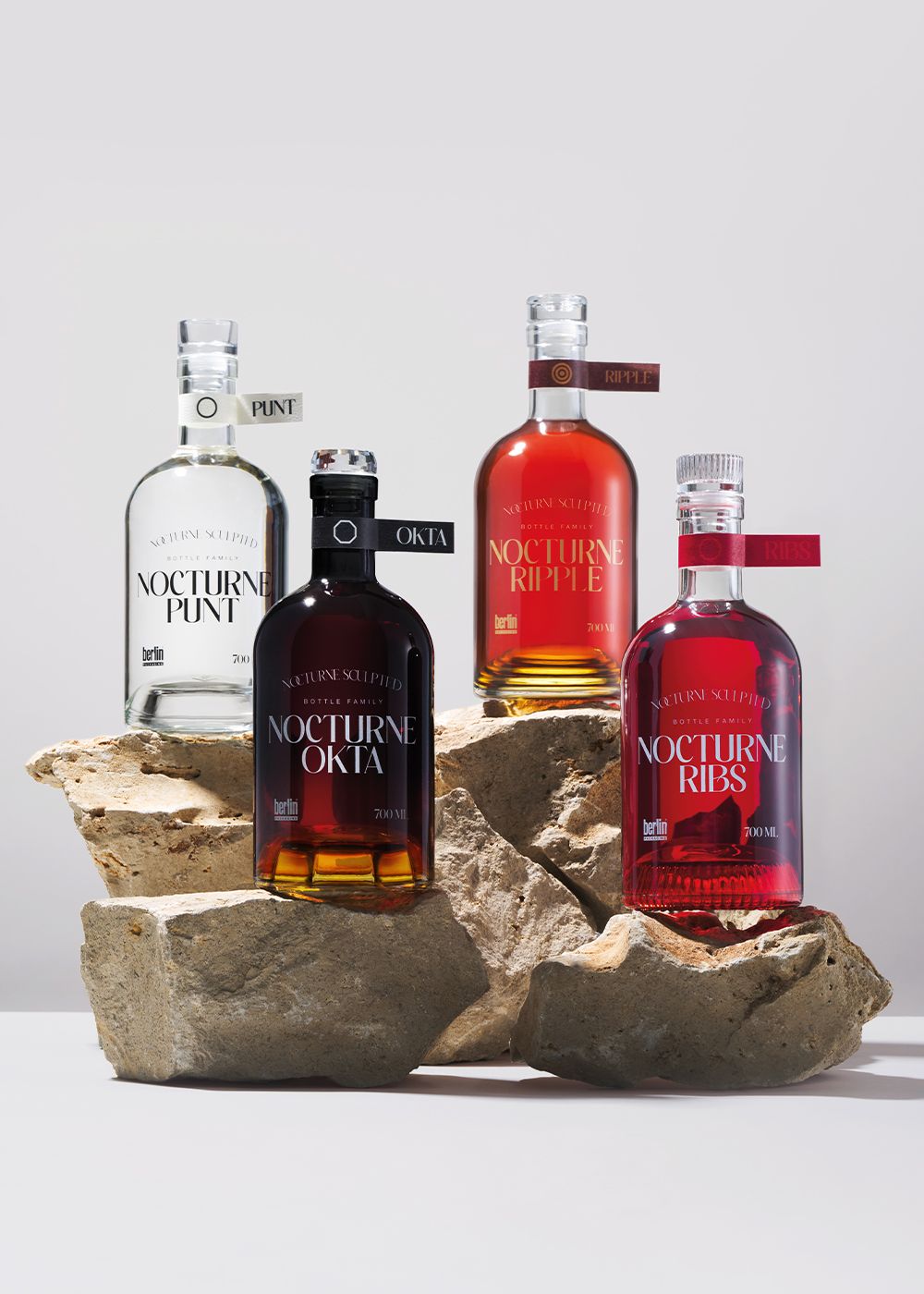 Four Nocturne bottles with label from sculpting collection: Punt, Okta, Ripple, and Ribs, displayed on rocks against a neutral background.