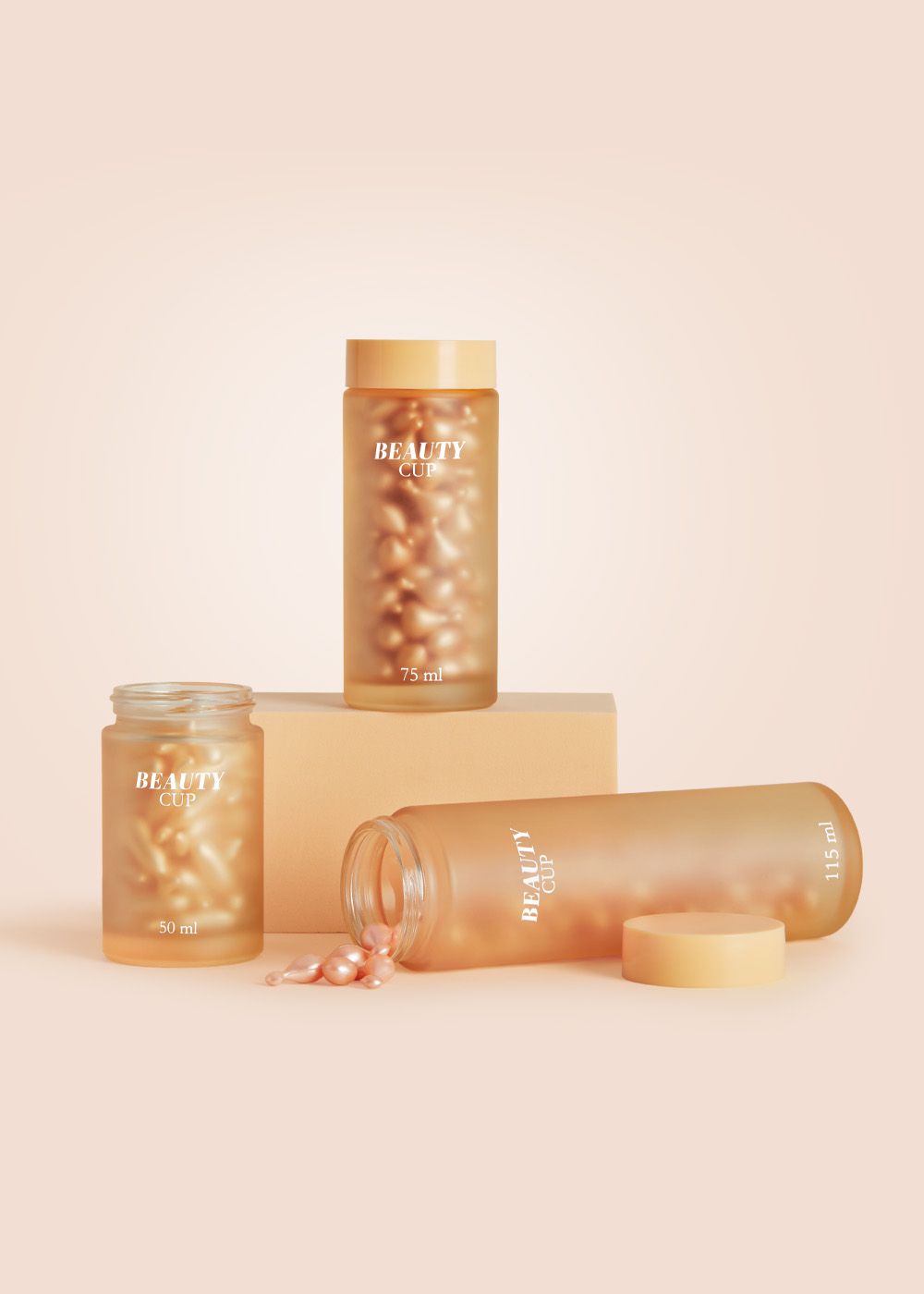 Three frosted cosmetic jars from BEAUTY CUP collection with gold caps containing capsules, in various sizes on a peach background.