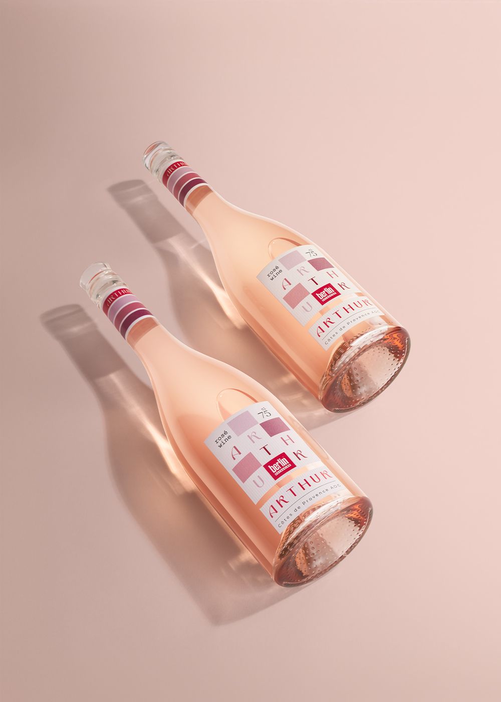 TwoArthur bottles filled with rosé wine with elegant labels, lying on a soft pink background, casting gentle shadows.