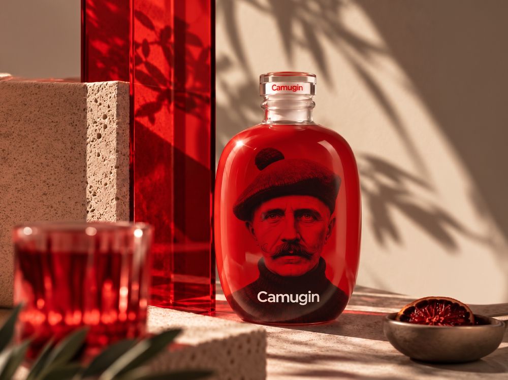 Stone bottle by Berlin Packaging for Camugin with red liquid, featuring an image of a man wearing a beret on the label, set against a textured surface.