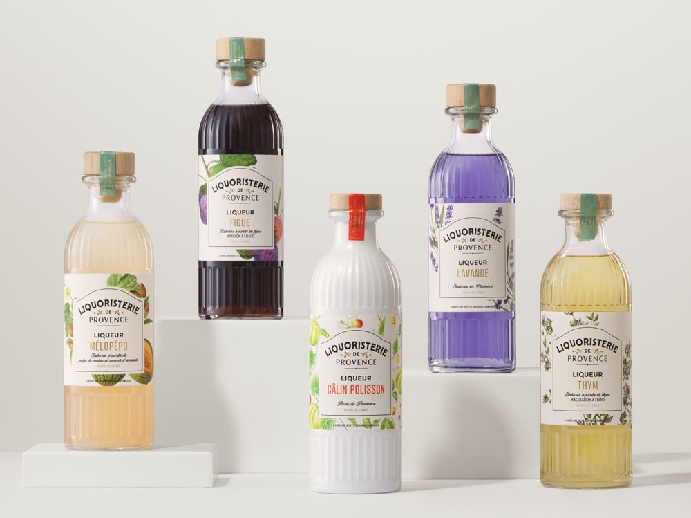 Five colorful bottles of Liquoristerie de Provence liqueurs with floral and herbal labels, each topped with corks and decorative bands.