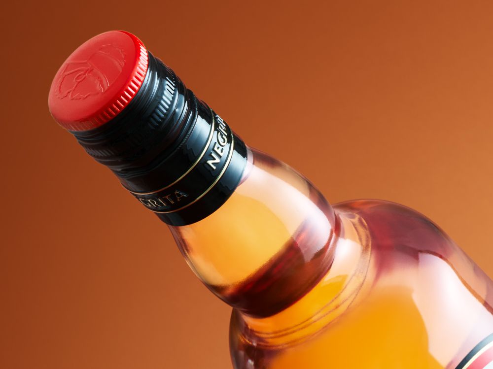 A close-up of Negrita Bardinet rhum bottle with a red cap and tilted to one side against a warm orange background.