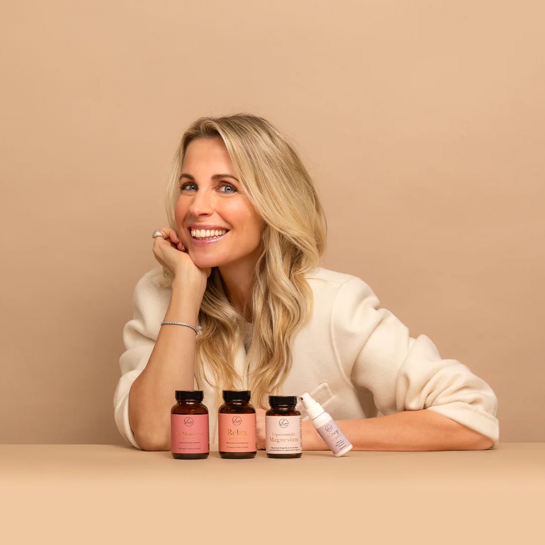 Smiling woman with long blonde hair poses with skincare products on a beige background.