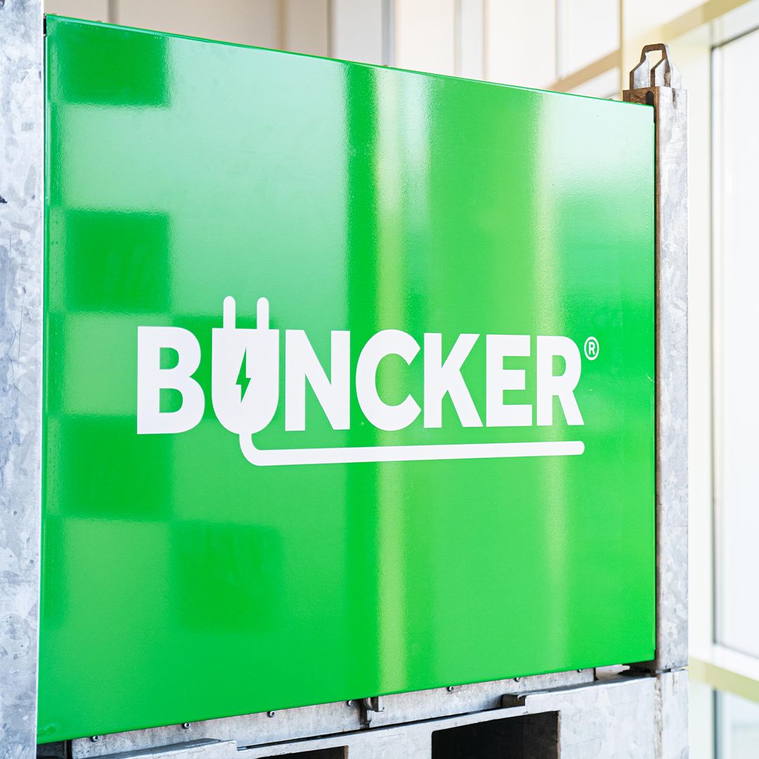 Green sign with white text "Büncker," featuring a plug icon, mounted on a metal frame.