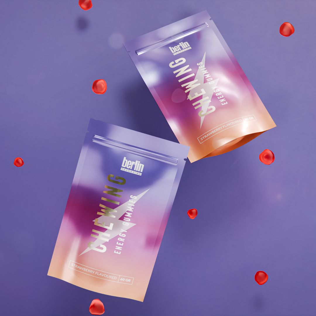 Two colorful packs of energy gummies with strawberry flavor on a purple background, surrounded by scattered red gummies.