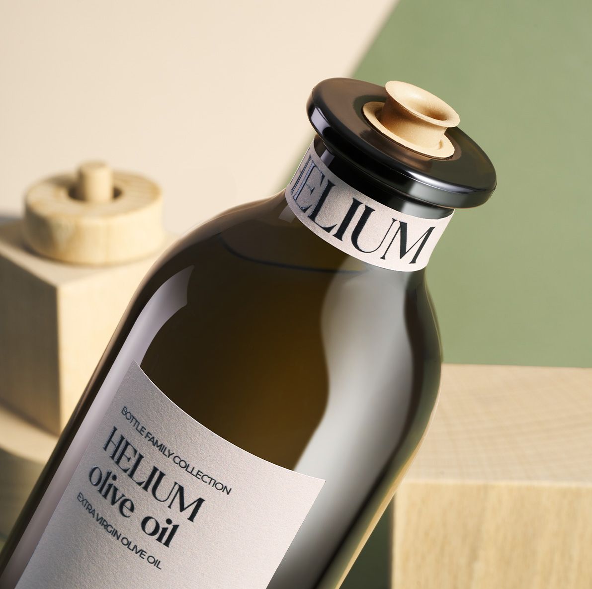Close-up of  Helium dark olive oil bottle with a wooden stopper set against a soft green and beige background.