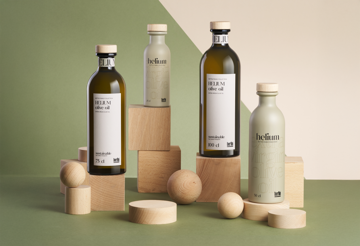 Collection of Helium olive oil bottles in sustainable packaging displayed with wooden blocks and spheres on a modern green and beige setting.