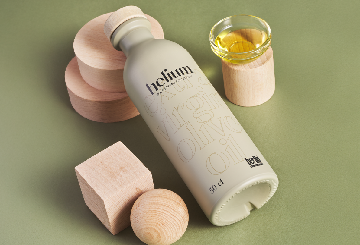 Premium Helium olive oil in matte light bottle with embossed typography, paired with a glass bowl of olive oil and wooden decorative elements.