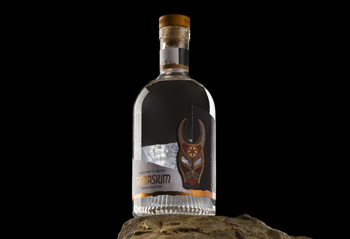 Nocturne Ribs glass bottle for spirits by Berlin Packaging customized by Redfish design agency, created for the Ginnasium project, featuring ribbed glass base, cork closure and shaped label with graphic illustration and hot stamping details, displayed on a rock.