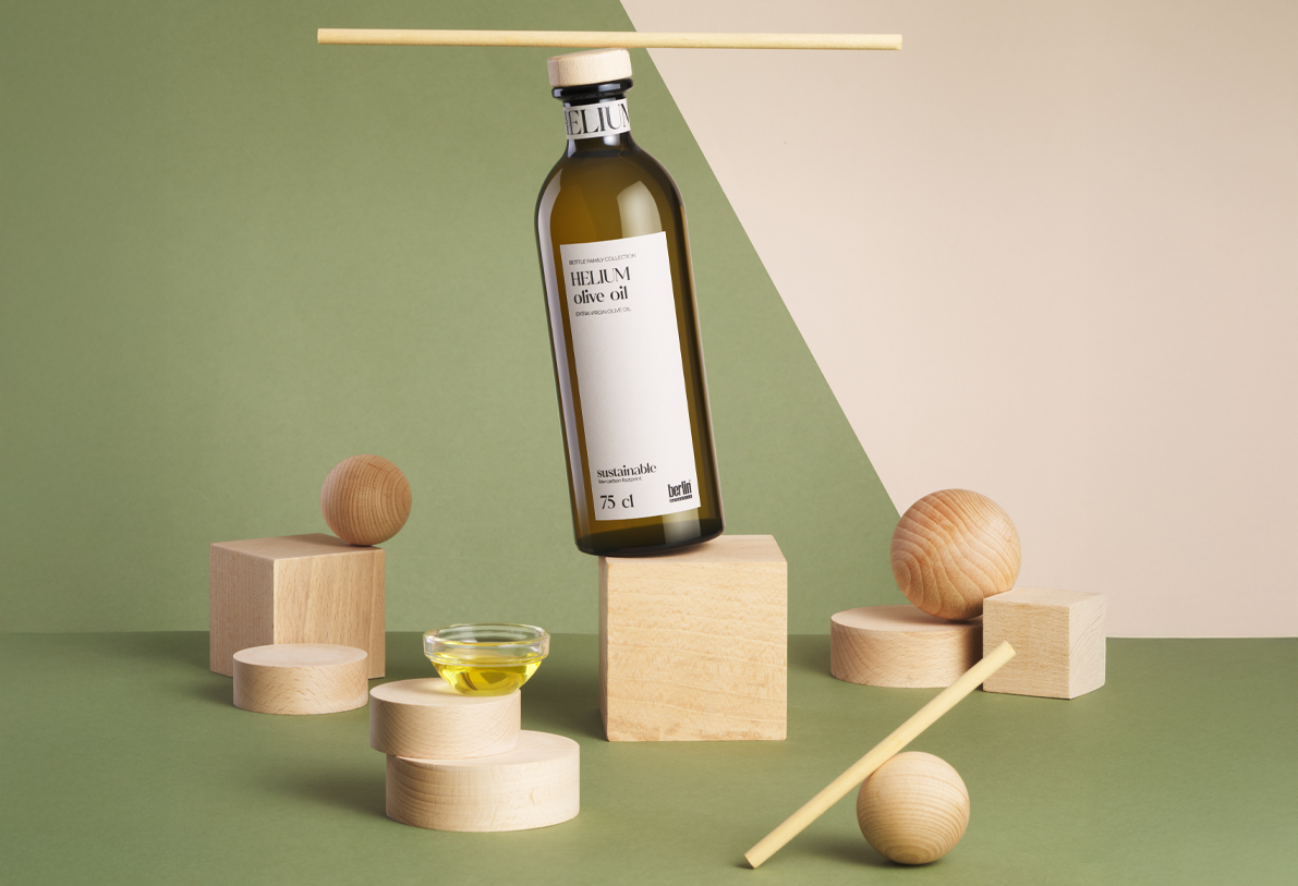 Helium extra virgin olive oil bottle balanced among wooden geometric shapes on a minimalist green and beige background.