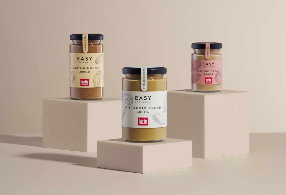 Three jars from the Easy Jar Family collection displayed on beige blocks: cashew cream (200 grams), pistachio cream (300 grams), and almond cream (100 grams).