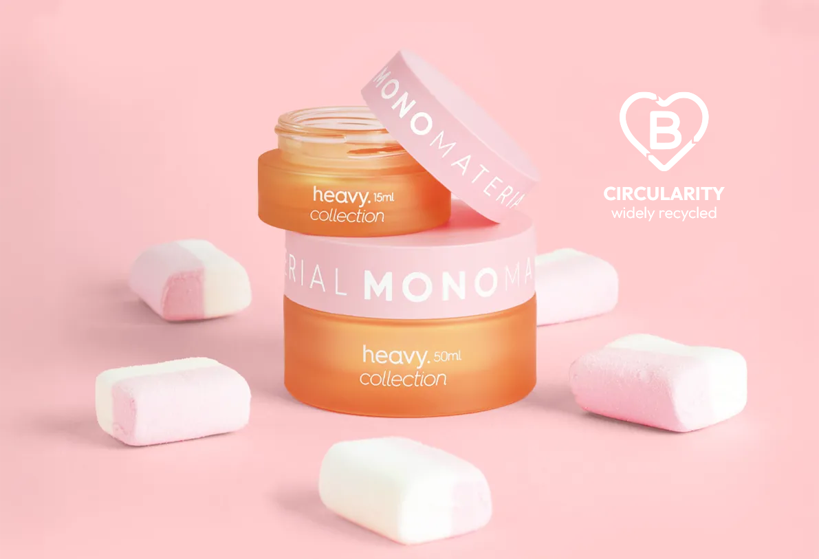 Two stacked orange cosmetic jars with pink lids labeled “heavy collection 15ml and 50ml,” surrounded by marshmallows on a pastel pink background.