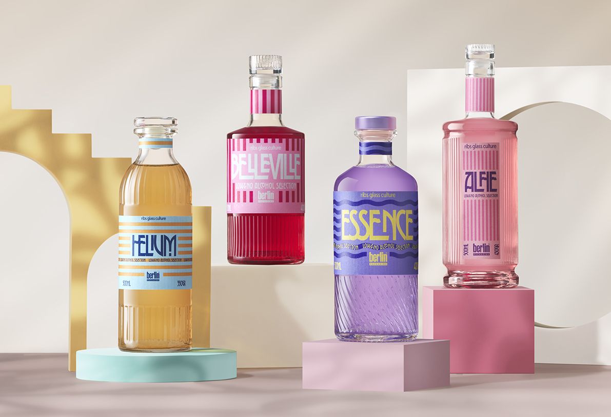 Berlin Packaging presents the Low & No Alcohol selection with four colorful bottles with vintage-style labels from the RIbs Glass Collection displayed on pastel geometric pedestals against a neutral background.