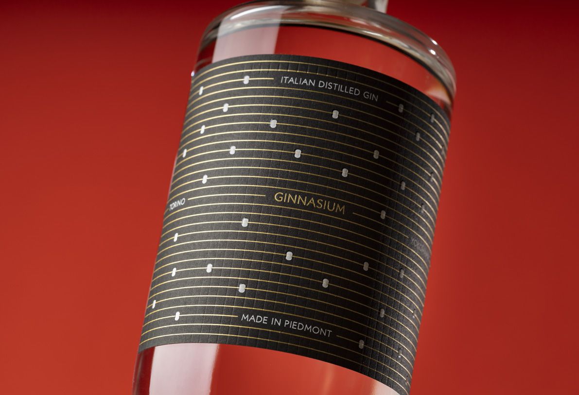 Close-up of a bottle of Jundo 700 glass bottle for spirits by Berlin Packaging customized by Mark Design, created for the Ginnasium project, with a black and gold design, against a red background.