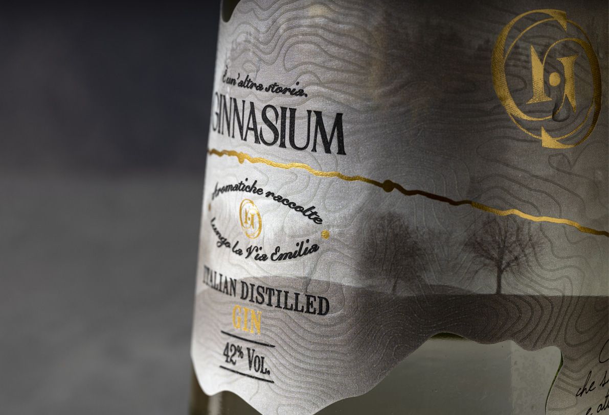 Alchemist 700 ml glass bottle for spirits by Berlin Packaging customized by Rewot creative agency, created for the Ginnasium project, close-up of shaped, textured label with hot stamping elements and typographic details.
