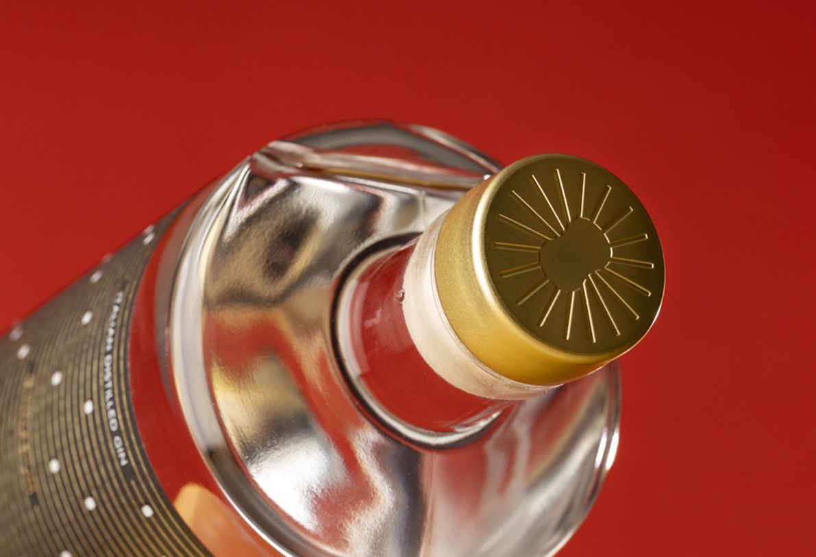 Close-up of a gold-embossed cap from Jundo 700 glass bottle for spirits by Berlin Packaging customized by Mark Design, created for the Ginnasium project, set against a vibrant red background.