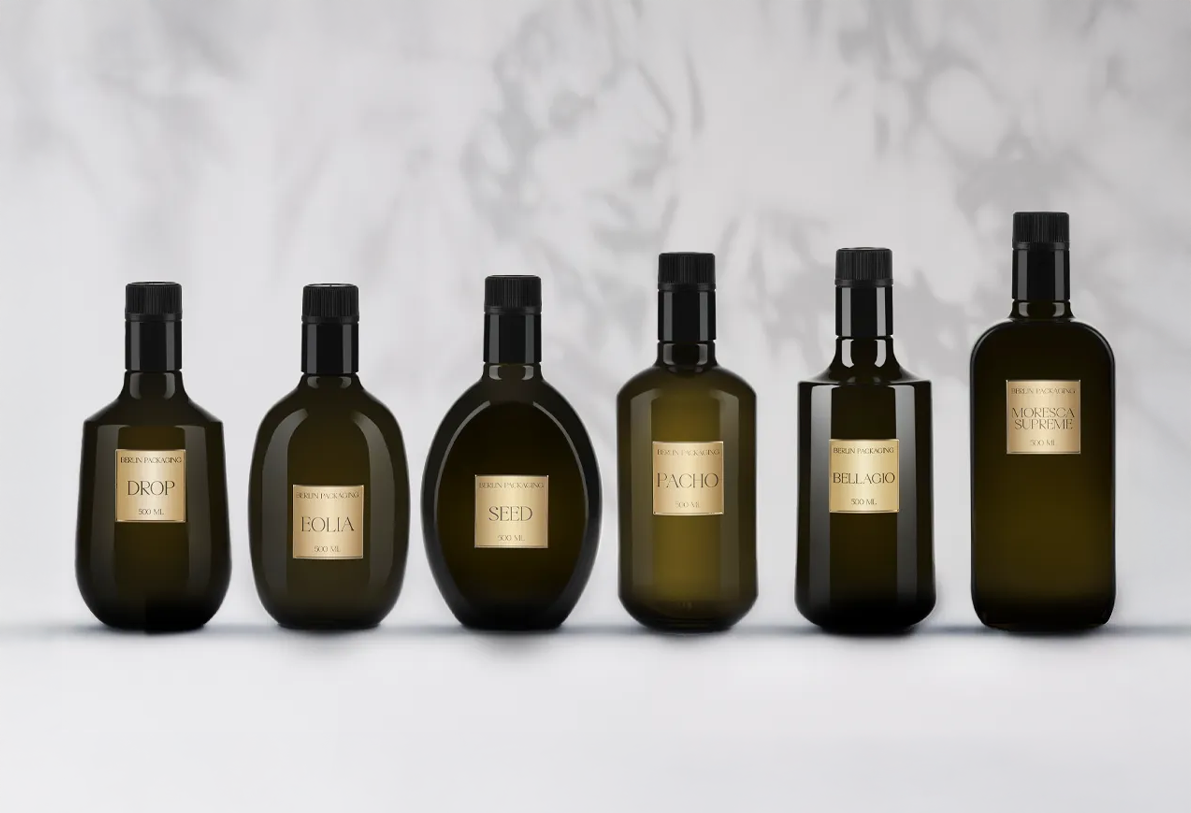 Six dark green glass bottles for oils, featuring black caps and gold labels, arranged in a row on a light background with soft shadows
