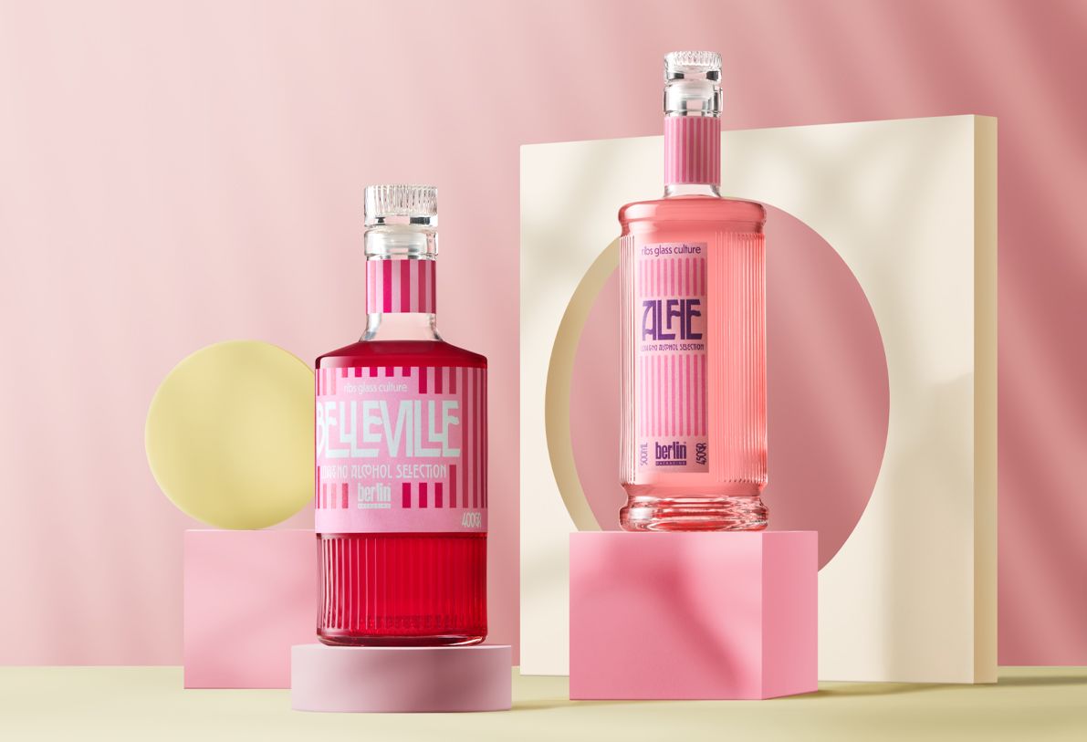 Two colorful, bottles Alfie Ribs and Belleville Ribs from the Ribs collection by Berlin Packaging filled with liquor on geometric pink and cream sculptures, set against a soft pink background.