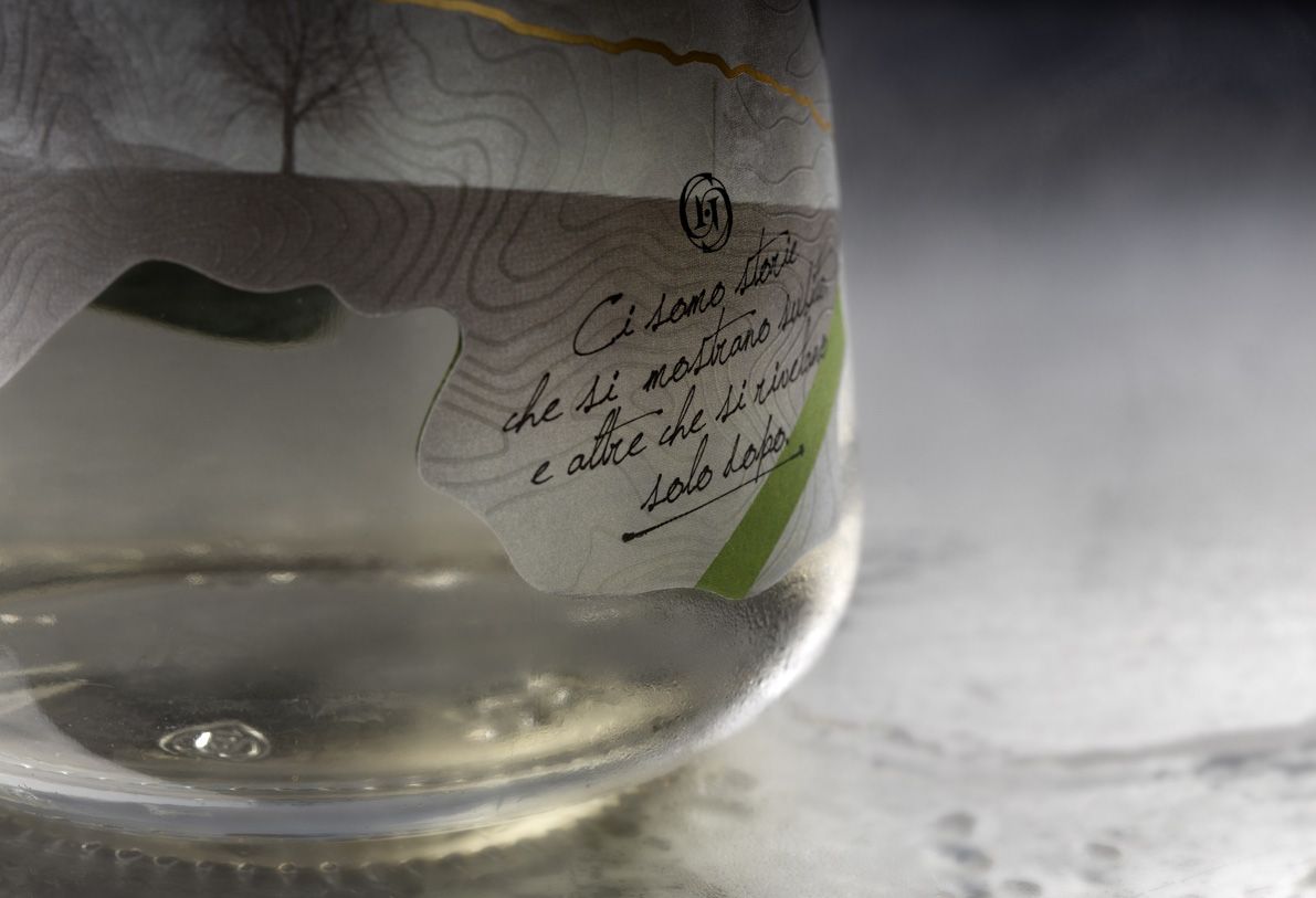 Alchemist 700 ml glass bottle for spirits by Berlin Packaging customized by Rewot creative agency, created for the Ginnasium project, detail of bottle base and shaped, textured label on the lower area.
