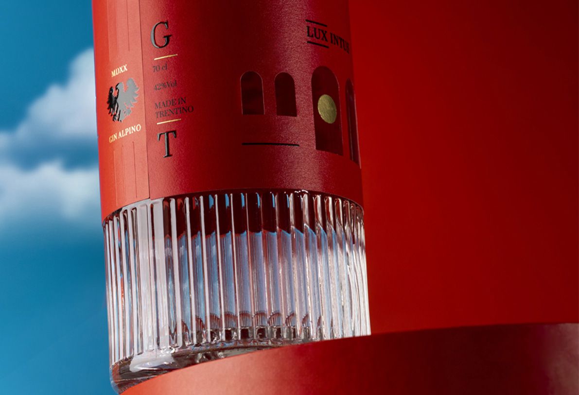 Belleville Ribs glass bottle for spirits by Berlin Packaging customized by Killer Idea, detail of textured glass base and red wrap label with cut-out elements, emphasizing material contrast and craftsmanship in the Ginnasium project.