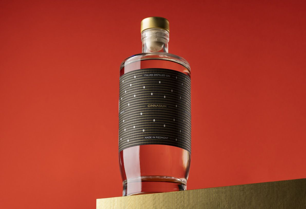 Jundo 700 glass bottle for spirits by Berlin Packaging customized by Mark Design, created for the Ginnasium project with a gold cap, set against a vibrant red background.