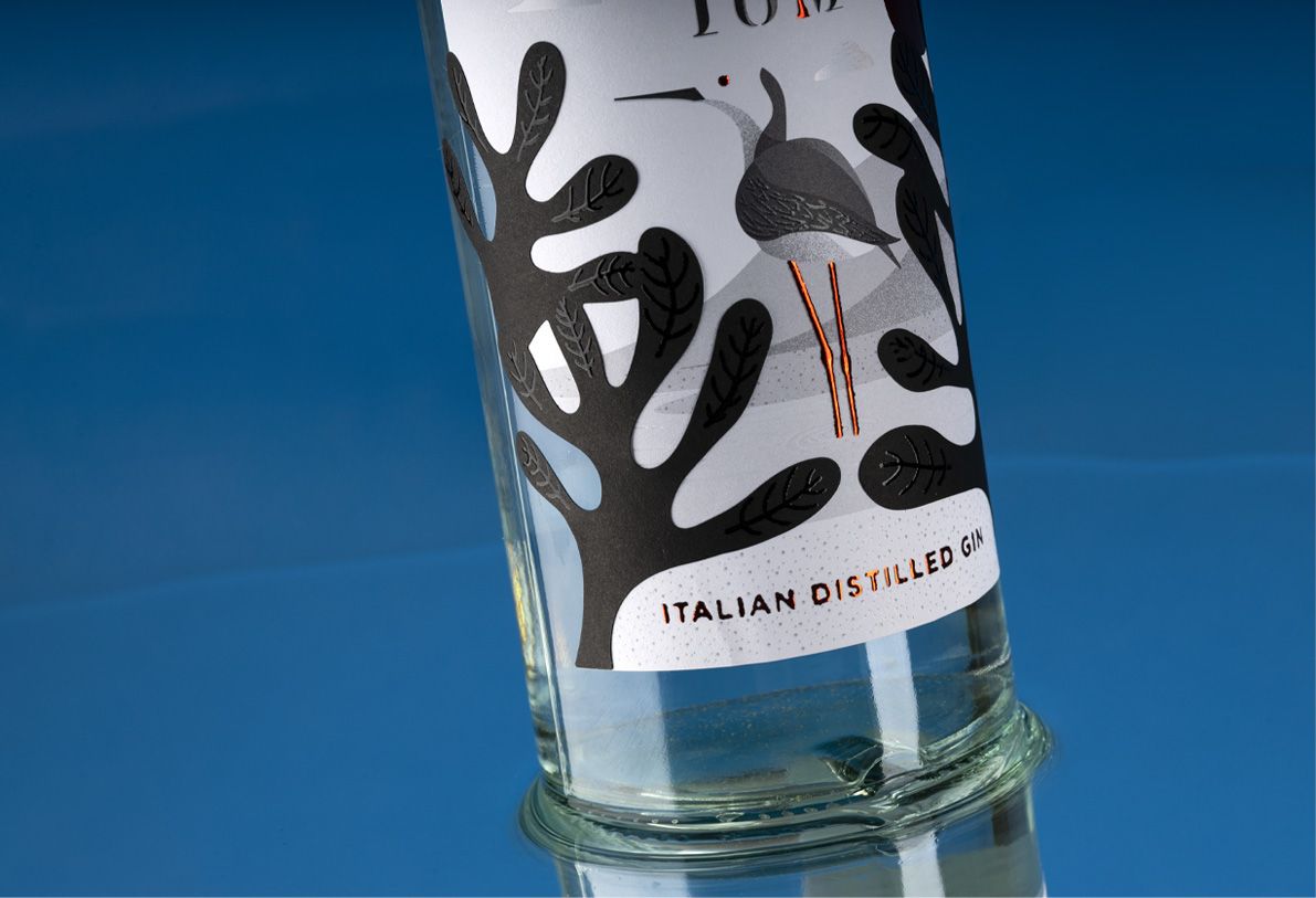 Helium Mixology 700 ml glass bottle for spirits by Berlin Packaging customized by Mark Design, created for the Ginnasium project, close-up of illustrated label with bird image and hot stamping details on graphic and typographic elements.