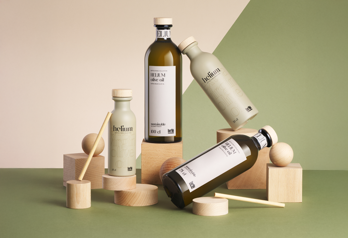 Artistic arrangement of Helium olive oil bottles in sustainable packaging with wooden geometric shapes on a green and beige background.