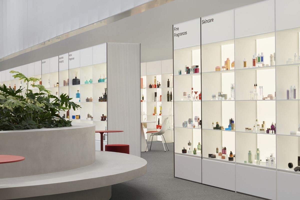 Modern store interior with white shelves displaying fine fragrances, skincare products, and decor items. Circular plant display in the foreground.