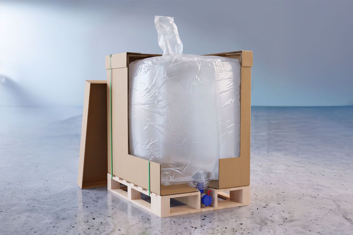 A large flexible container in a cardboard box on a wooden pallet, with a blue dispensing valve at the bottom, placed on a gray surface.